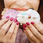 Unrecognizable young woman eating delicious donuts.
