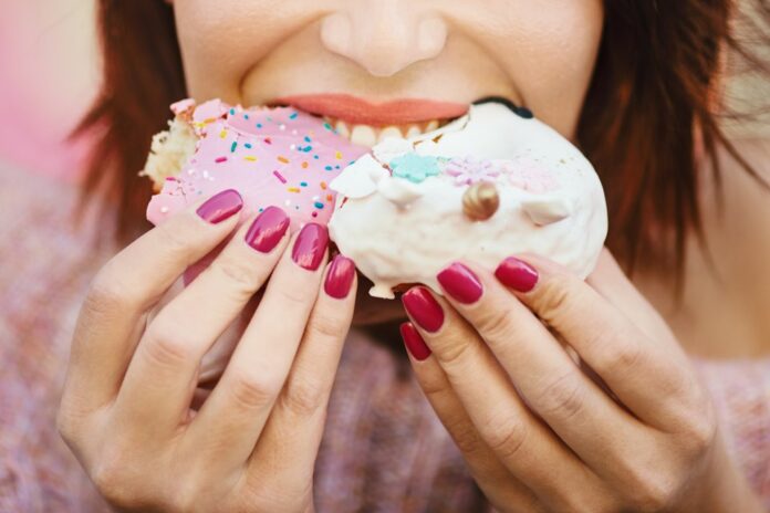 Unrecognizable young woman eating delicious donuts.
